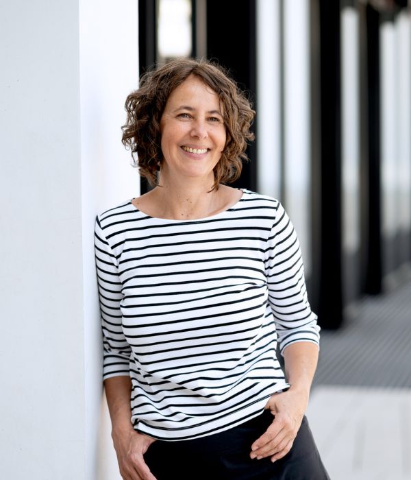 Portrait Katrin Behr: lächelnd, stehend, schwarz/weiß gestreiftes Shirt vor schwarz/weißem Hintergrund